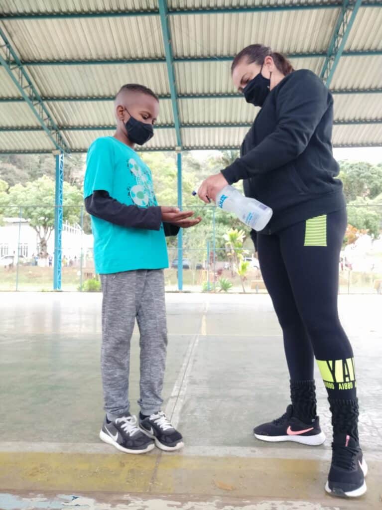 Instituto Mais Ação - Aulas presenciais em Juiz de Fora - professora colocando álcool na mão do beneficiado